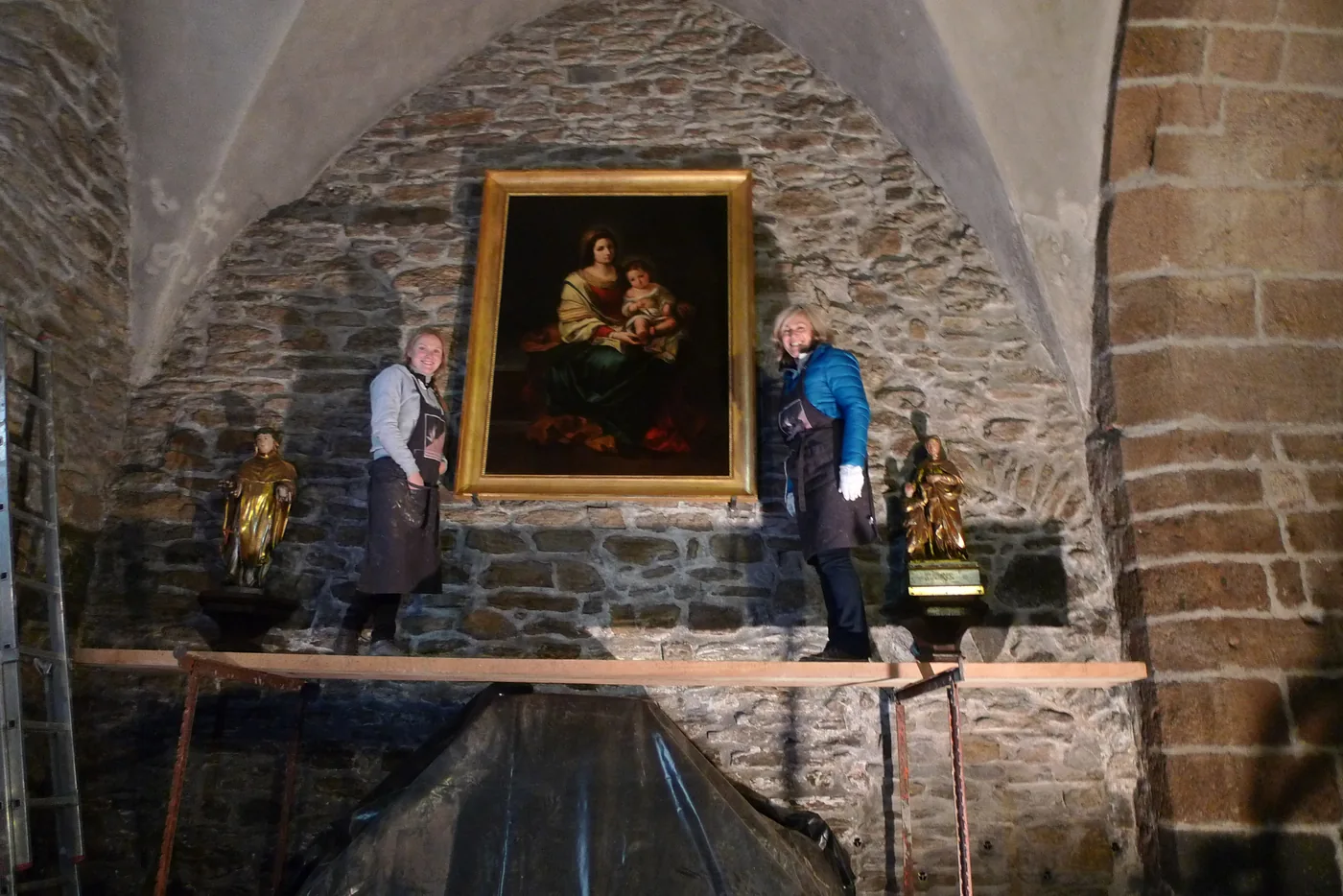 Deux restauratrices sur un échafaudage, devant un tableau accroché dans une église