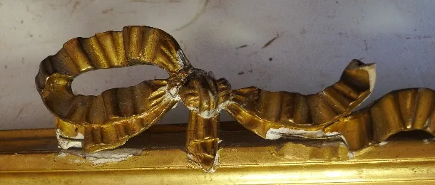 Nœud de ruban doré sur un cadre, cassé : une boucle manque, le blanc apparaît